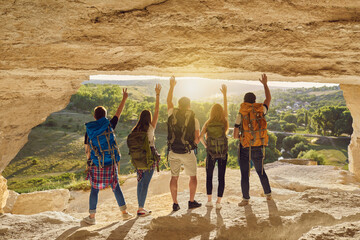 Wall Mural - group of travelers with backpacks standing at the cave entrance and admiring the view
