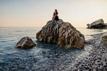 Girl In Black Dress Posing At Sunset On The Rock At Sea