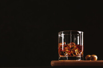 Whiskey in a glass with ice. On the right are two olives. Serve on a wooden board. On a black background, space for text.