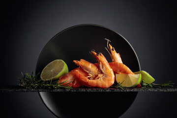 Prawns with rosemary and lime on a black plate.