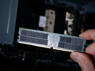 Male hand holding computer RAM random access memory with computer workstation in the background