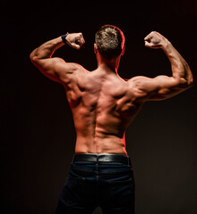 Handsome sexy man with athletic body showing muscular back and arm biceps standing isolated on black background. Sport, bodybuilding motivation. Dark studio shot copy space portrait