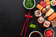 Various Types Of Sushi On A Blue Round Plate, Wakame Chuka Salad, Soy Sauce In A Bowl, And Ginger On The Side. Asian Food Composition On Stone Background, Top View, Copy Space