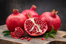 Healthy Pomegranate Fruit With Leaves And Open Pomegranate On An Old Wooden Board, Side View, Dark Vintage Background.