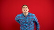 © Vital9c - A young man has a backache and is holding it in his hands. Shooting on a red background.