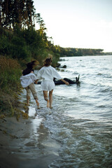 Wall Mural - two young women hold hands and run barefoot along the beach at sunset. two girls run away