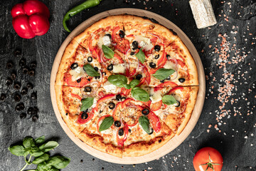 Hot tasty traditional italian pizza with salami, meat, cheese, tomatoes greens on a dark background