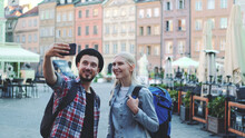 Happy Young Couple Of Tourists Making Selfie On Smartphone In The City Center. They Have Tourists Bags.
