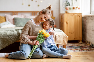 daughter congratulating mother with flowers at home