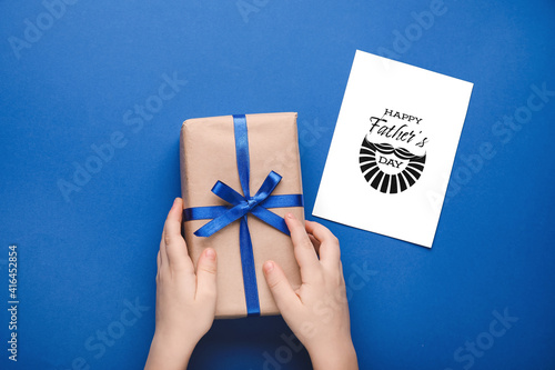 Hands with gift for Father\'s Day and greeting card on color background