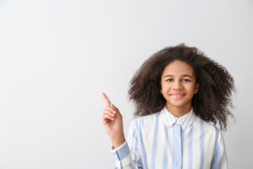 Wall Mural - African-American teenage girl pointing at something on light background