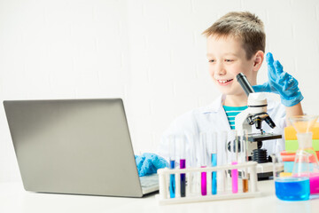 Wall Mural - schoolboy with a laptop in the laboratory conducts chemical experiments with substances in test tube