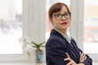 © ALEKSEI - young strict business woman in a blue jacket and glasses is thinking at the window in the office at her workplace