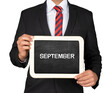  A Businessman holding slate mini blackboard with message September