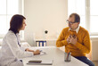 © Studio Romantic - Middle aged man talking to doctor and complaining about chest pain during health exam at hospital. Professional general practitioner interviewing adult male patient sitting at desk at her office