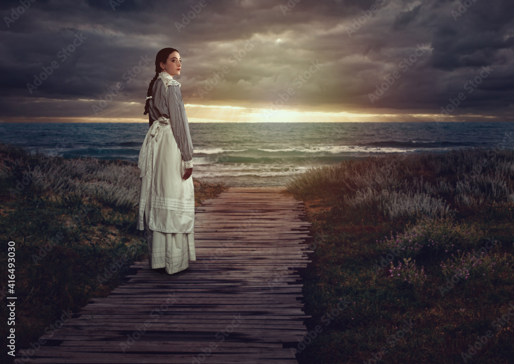 Young victorian girl in white dress and blue striped blouse on a boardwalk at the coast at sunset. - obrazy, fototapety, plakaty 