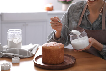 Sticker - Young woman decorating traditional Easter cake with glaze in kitchen, closeup. Space for text