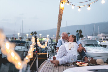 Wall Mural - Senior couple having tender moment on boat while drinking champagne and eating fruits - Focus on faces