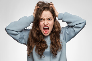 The young woman is angry and screaming, holding her head. Young girl with long hair and blue clothes.