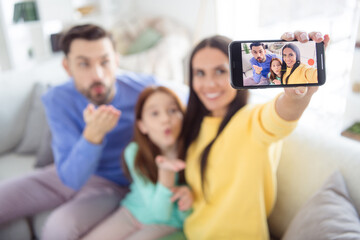 Poster - Photo of young cheerful family mom make selfie smartphone dad daughter send air kiss happy positive smile sit sofa home