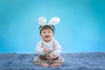 baby in easter bunny hairband. asian happy baby smiling and sitting on carpet on blue background. cu