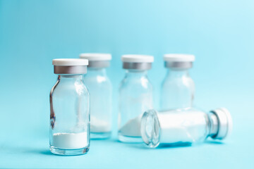 Glass vials with medicine in powder form on blue background, soft focus