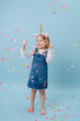 © zzzdim - Happy little blonde girl in unicorn head band and jeans overalls stretching over blue background.