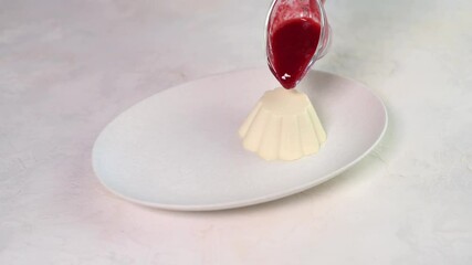 Wall Mural - Woman's hand pours raspberry syrup panna cotta on oval white plate, close up, 4k resolution