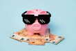 Pink piggy money bank with black sunglasses and euro bills