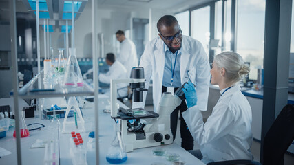 Wall Mural - modern medical research laboratory: two scientists working together using microscope, analysing samp