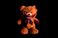 Scary Bear With A Creepy Bloody Grin On A Black Background. Horror Toy. Halloween Concept. A Severed Paw And A Bitten Off Ear Covered In Blood