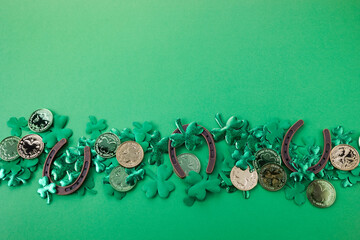 St Patricks Day border of shamrocks and gold coins and horseshoe over a green background. Top view, flat lay.