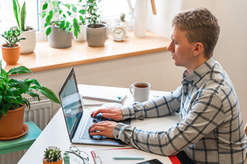 Wall Mural - a man in a shirt sits in a modern office and uses a laptop to work in business or programming, appli