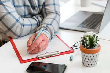 Canvas Print - a young man in a shirt in a bright office works at a laptop and makes notes in a notebook, the menta