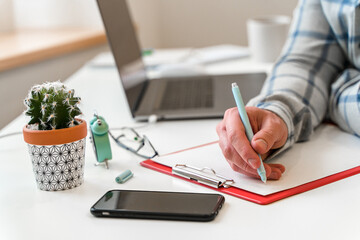 Canvas Print - a young man in a shirt in a bright office works at a laptop and makes notes in a notebook, the menta