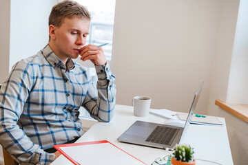 Canvas Print - a young man in a shirt in a bright office works at a laptop and makes notes in a notebook, the menta