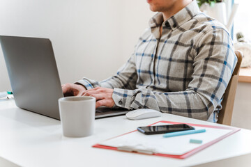 Wall Mural - handsome man working using computer laptop and drinking a mug of coffee with thinking serious face i