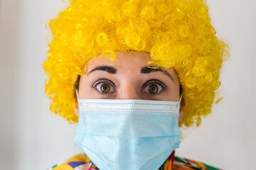 Linda mujer joven sonriendo mientras está vestida con un disfraz de payaso con una mascarilla quirúrgica desechable y una peluca de payaso amarilla. Protección contra el virus sars-cov-2