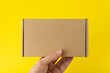 Hand holds rectangular cardboard box, yellow background. Copy space. Mock up.