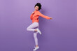 Full length view of glad chinese girl standing on one leg. Studio shot of carefree asian female model dancing on purple background.