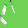 Vaccine Bottles And Needle Syringe On Green Background. Covid Pharmaceutical Glass Vials Containers. Immunity Injection Concept.