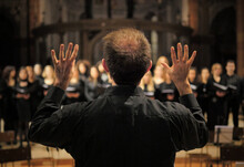 Musician Leads A Choir During A Concert In A Cathedral. Musical Rehearsals Before The Concert During The Christmas Period. Life Of Musicians And Classic Holy Music.