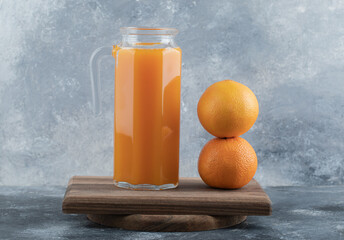 Fresh juice and two oranges on wooden board