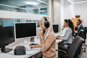 Wall Mural - Beautiful blond smiling female call center worker accompanied by her team working in the office.