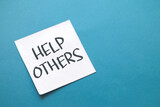 Fototapeta  - Help others, text words typography written on paper against blue background, life and business motivational inspirational