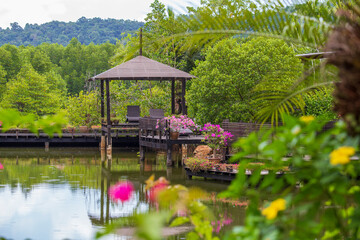 Wall Mural - Wooden gazebo with sun loungers for relaxing on a terrace with flowers next to a lake on the tropical island of Thailand