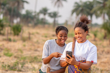 two female african farmers viewing content on a phone together, feeling excited