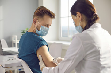 Man in medical face mask getting injection at hospital. Doctor or nurse holding syringe and giving shot to male patient. Global pandemic. New Covid-19 vaccine clinical trial. Immunization campaign