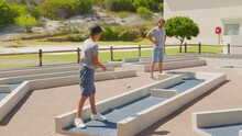 Man With His Son Playing Mini Golfers On Mini Golf Course At Summer Day.