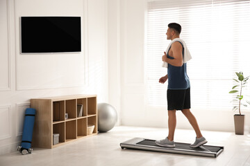 Canvas Print - Sporty man training on walking treadmill while watching TV at home